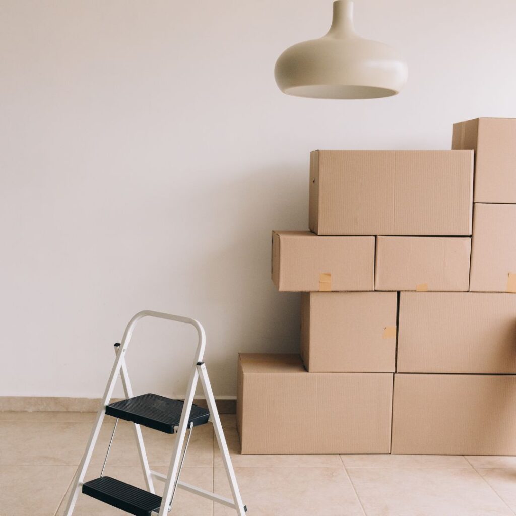 Stacked moving boxes beside a step ladder in a clean, neutral room.